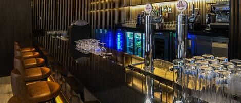 A bar area with a long counter, multiple stools, and a well-stocked shelf with various bottles.