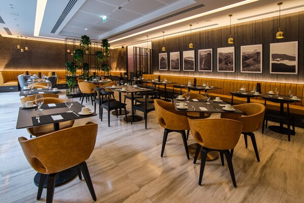 Un restaurante moderno con paneles de madera, sillas negras y amarillas, y mesas dispuestas para comer.