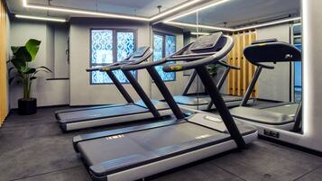 Een fitnessruimte met loopbanden, een potplant en raampartijen met een patroon.