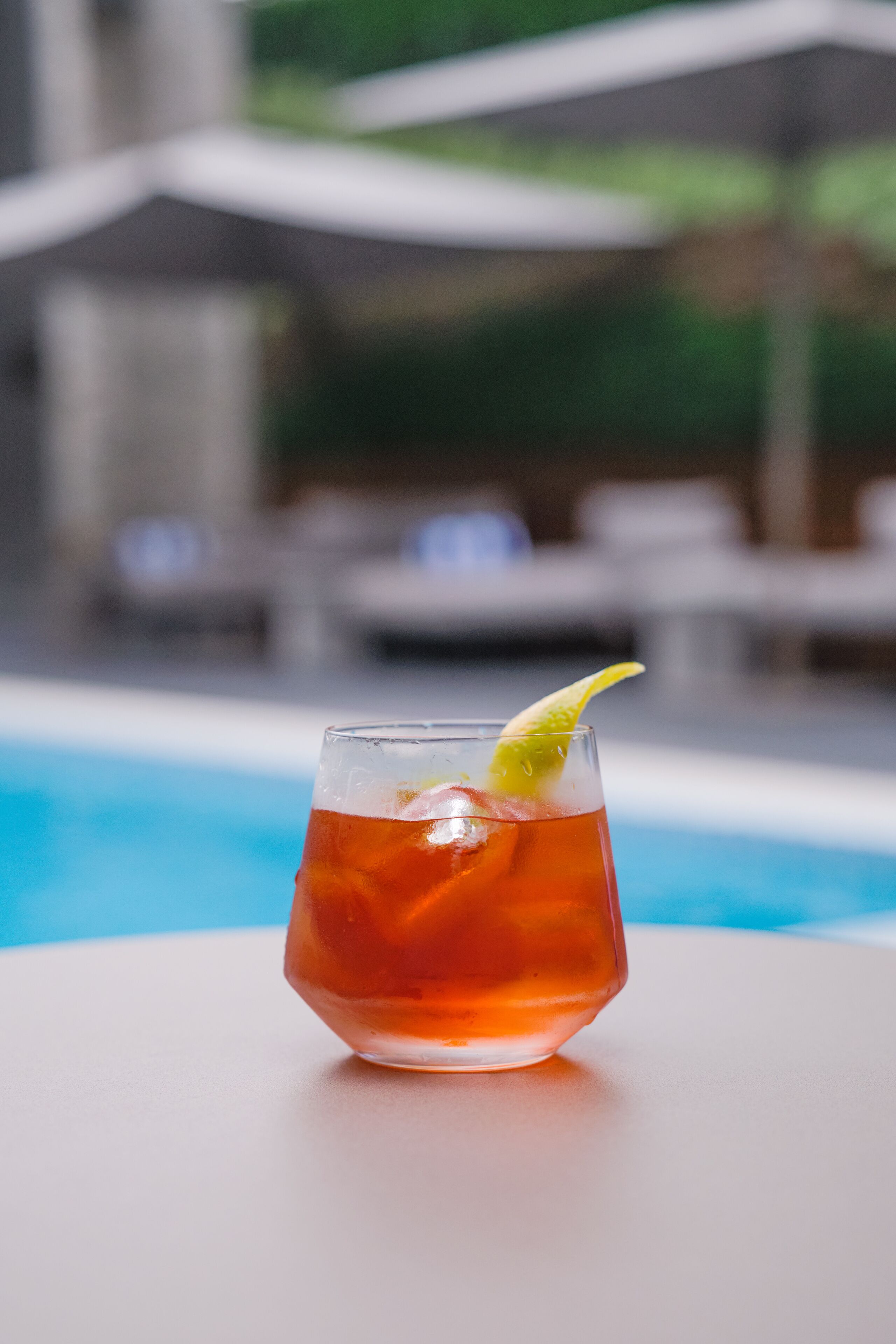 Ein Glas rotes Getränk mit Limettenscheibe auf weißer Oberfläche in Poolnähe.