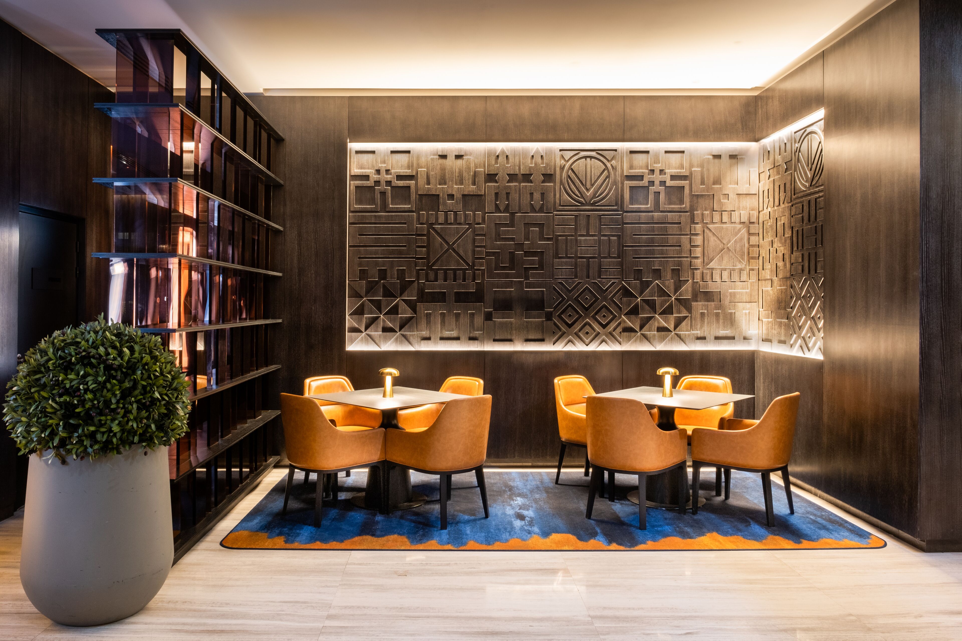 Een moderne bibliotheek met boekenplanken, een decoratieve wand en een zithoek met tafels en stoelen.