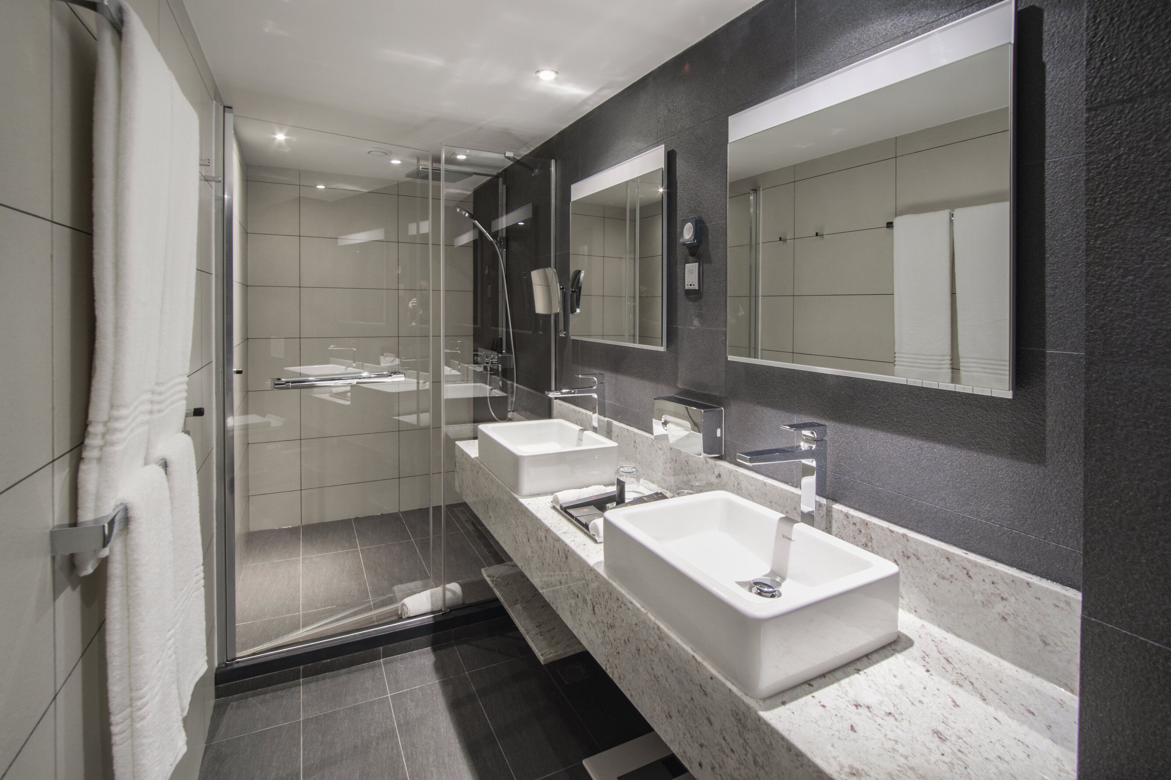 A modern bathroom with three sinks, a large mirror, and a glass shower enclosure.