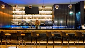 A bar area with a marble countertop, multiple bar stools, a variety of bottles, and a flat-screen TV mounted on the wall. - K Hotel Douala (Douala)