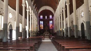 A church interior with rows of wooden pews, white columns, and stained glass windows.