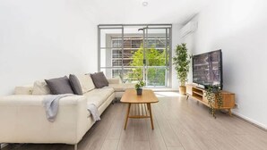 Una sala de estar moderna con un sofá, una mesa de centro, un televisor y un ventanal con vistas a zonas verdes.