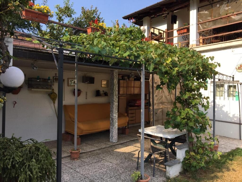 Un espacio al aire libre cubierto con una mesa y sillas, una pérgola con plantas trepadoras y un edificio con balcones y ventanas.