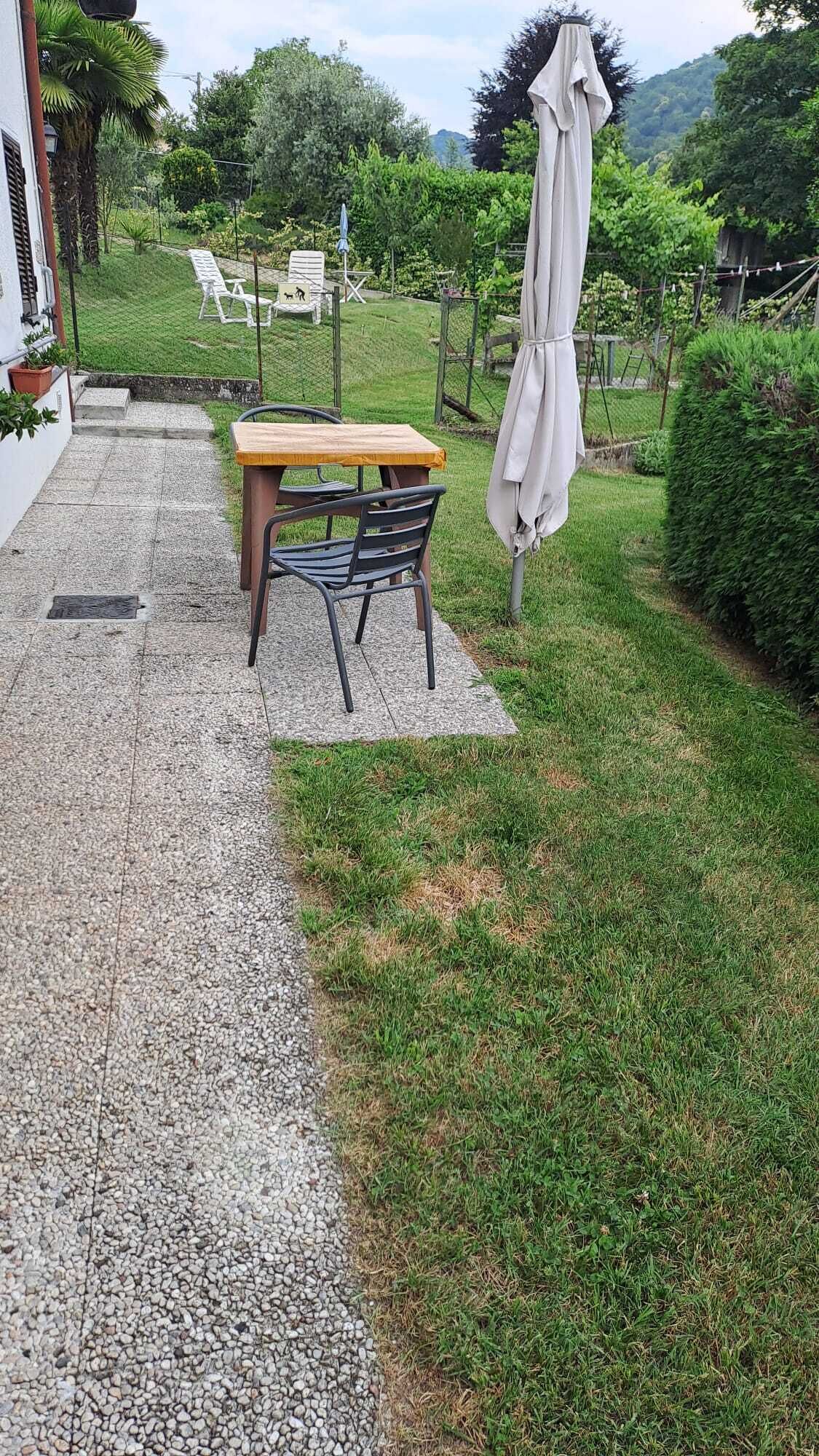 A patio with a table and chairs, a hanging umbrella, and a garden with a fence and greenery.