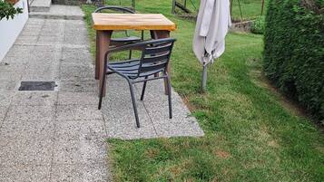 A patio with a table and chairs, a hanging umbrella, and a garden with a fence and greenery.
