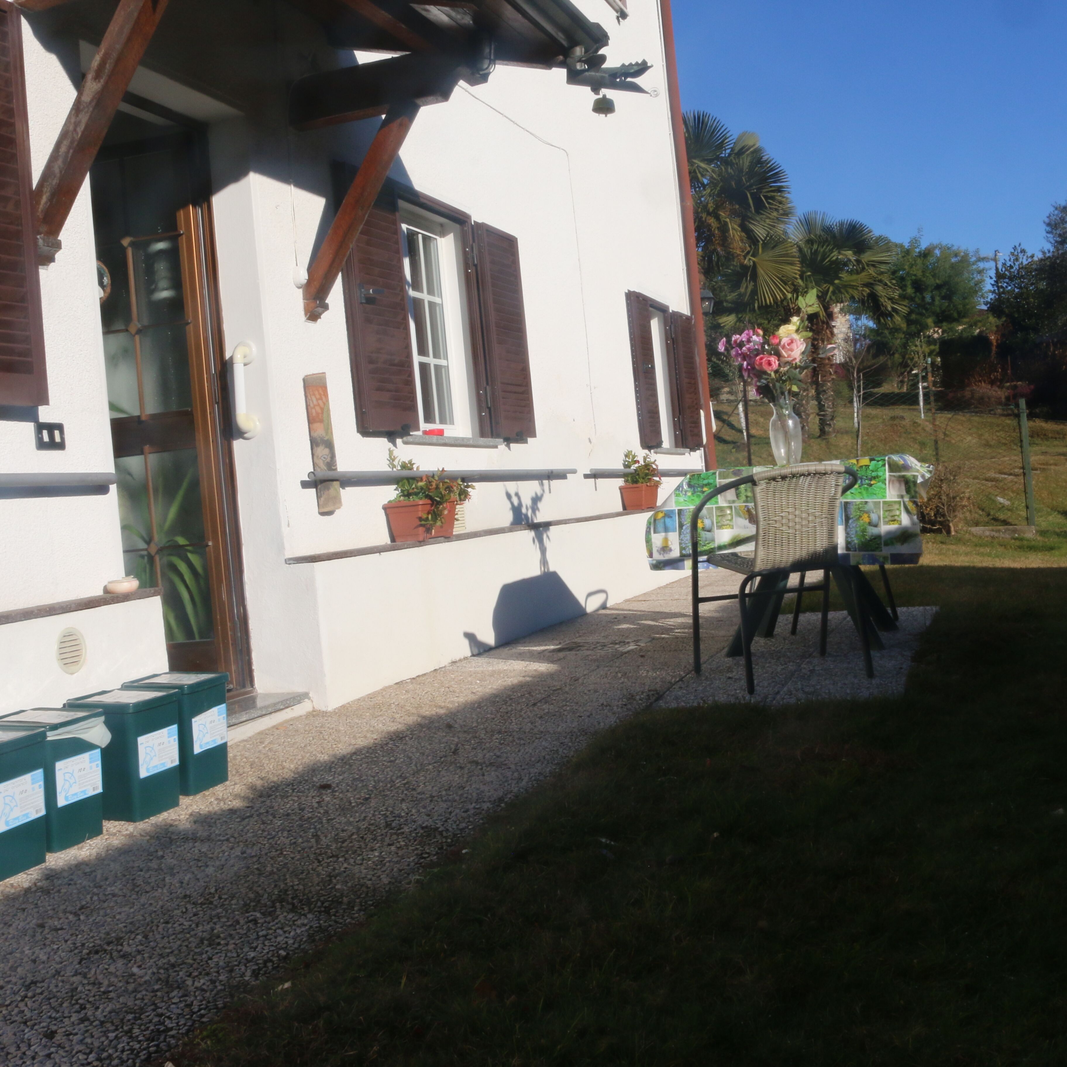 A white building with wooden shutters, a balcony with potted plants, and a table with chairs outside.