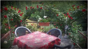 Ein Tisch mit einer blumigen Tischdecke, zwei Stühle und ein Garten mit roten Rosen.