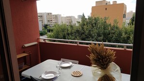 Ein Balkon mit einem Tisch für zwei Personen, einer Vase mit Trockenpflanzen und Blick auf Gebäude und Grünflächen.