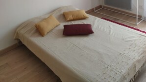 Ein Schlafzimmer mit einem Bett, einem Nachttisch, einem Heizkörper, einer Topfpflanze und einem an der Wand befestigten Regal.