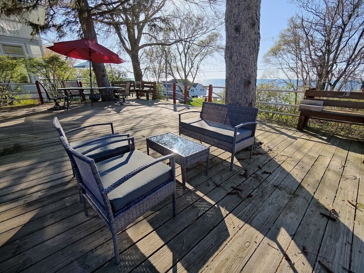 A wooden deck with wicker furniture, a red umbrella, and a view of the sea.