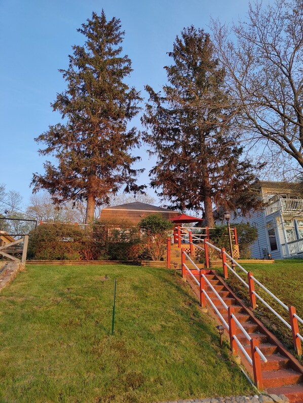 A staircase leading up to a building with a red roof, surrounded by trees and a grassy area.