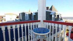 Un balcón con una mesa azul y barandilla blanca con vistas a una playa.