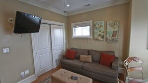 Una sala de estar con una televisión de pantalla plana montada en la pared, un sofá con cojines rojos, una mesa de centro de madera y un ventilador de techo.