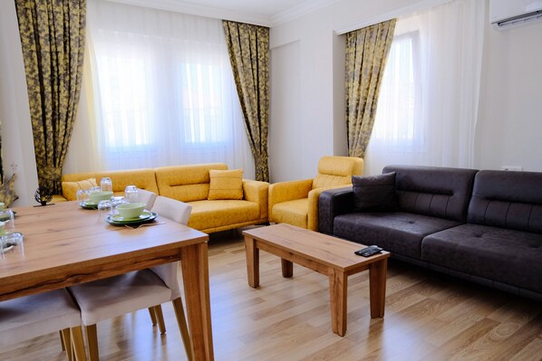 A living room with a wooden dining table, yellow and grey sofas, and a dark grey couch. - Ozgur City Residence (Fethiye)