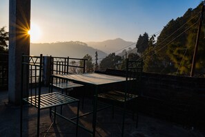 A terrace with metal tables and chairs, overlooking a mountainous landscape with a clear sky.