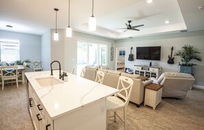 A spacious living area with a large island, a ceiling fan, and a TV mounted on the wall.