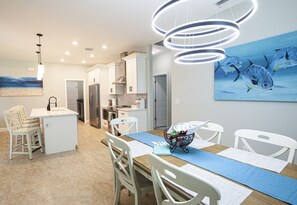 A modern kitchen with white cabinetry, a central island, and a dining area with white chairs and a blue rug.
