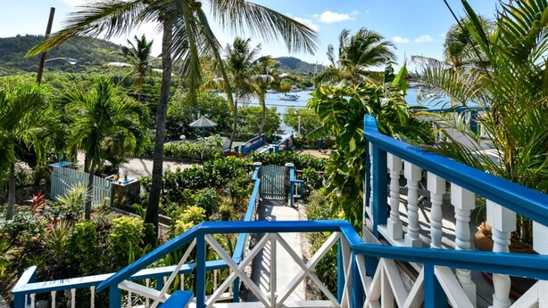 A tropical resort with a staircase leading to a pool area, surrounded by palm trees and a view of the ocean.