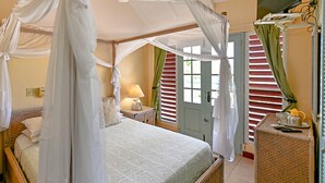 A bedroom with a four-poster bed, a nightstand with a lamp, and a wicker chair.