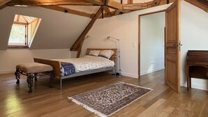 Un dormitorio con techo inclinado, una cama, un banco, un tapete y un armario de madera.
