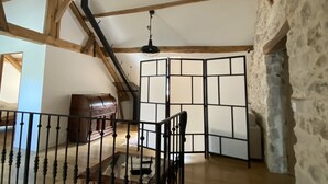 Una habitación con una escalera de madera, un piano y una pared de piedra.