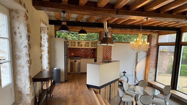 Una cocina moderna con una isla central, vigas de madera y un comedor con mesa y sillas de vidrio.
