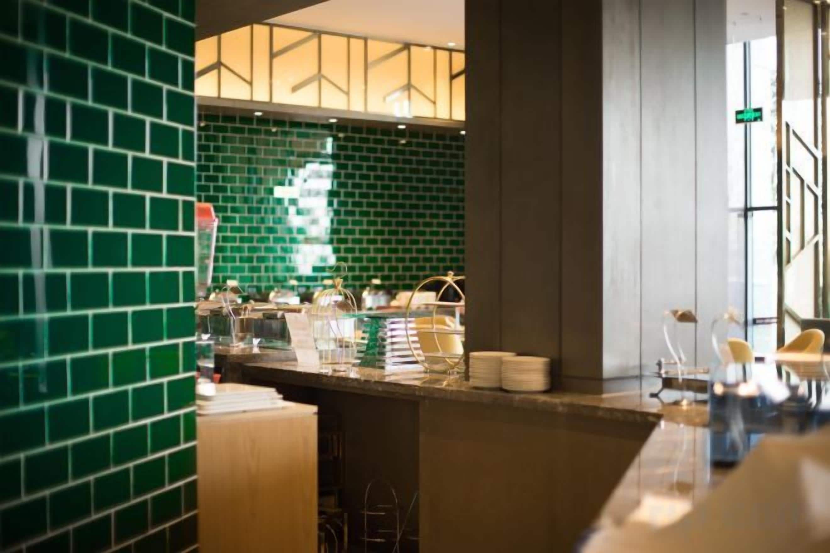 A hotel lobby with a green-tiled wall, a reception desk, and a seating area.