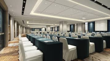 A conference room with rows of tables and chairs, a large screen, and a carpeted floor.
