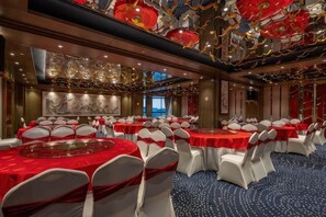 Un salón de banquetes con mesas redondas, sillas blancas y manteles rojos.
