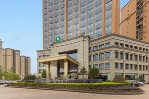 A multi-story building with a prominent entrance and a green logo on the facade.