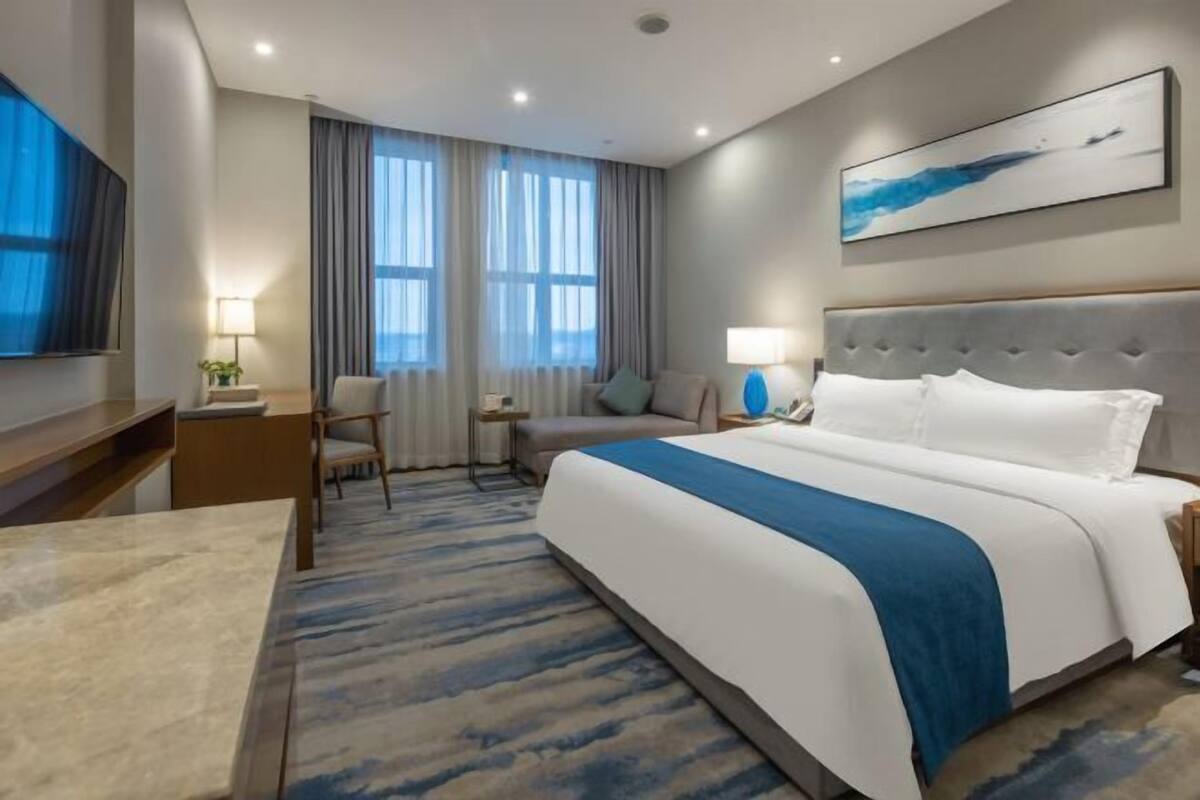 A hotel room with a large bed, a desk, a chair, a TV, and a window with curtains.