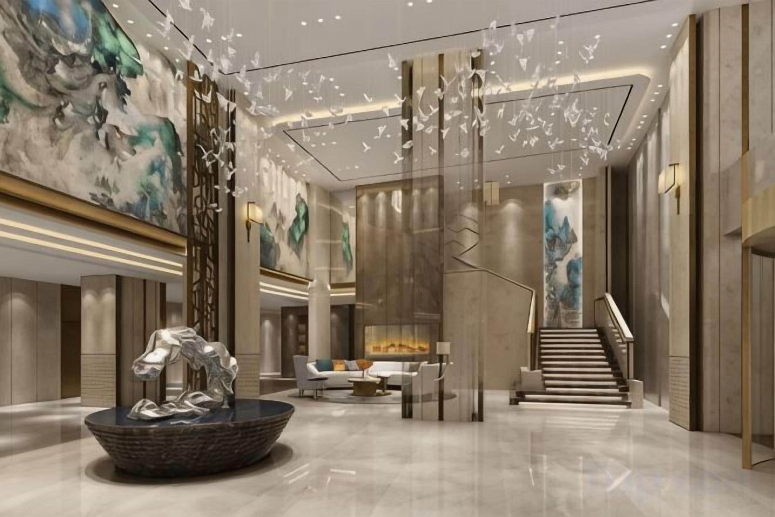A modern lobby with a central fountain, a staircase, and a large abstract painting on the wall.