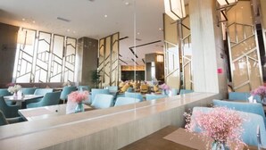 Een moderne hotelentree met een lange receptiebalie, blauwe zitplaatsen en decoratieve bloemarrangementen.