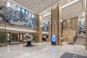 A spacious lobby with a marble floor, a central sculpture, and large wall murals.