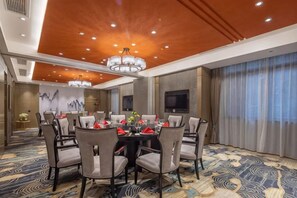 Une salle de conférence équipée d’une table ronde, de chaises, d’un lustre, d’un téléviseur à écran plat et d’un tapis à motifs.
