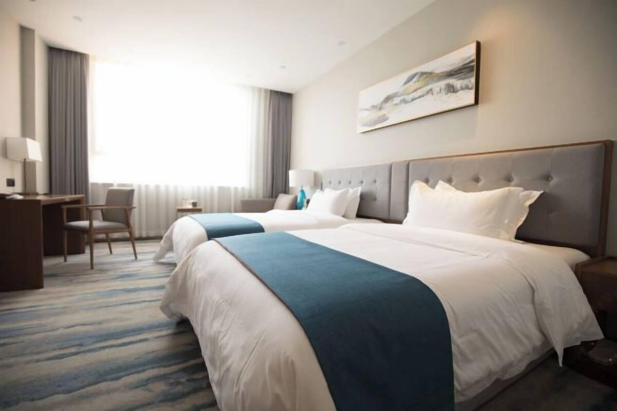 A hotel room with two beds, a desk, a chair, and a painting on the wall.