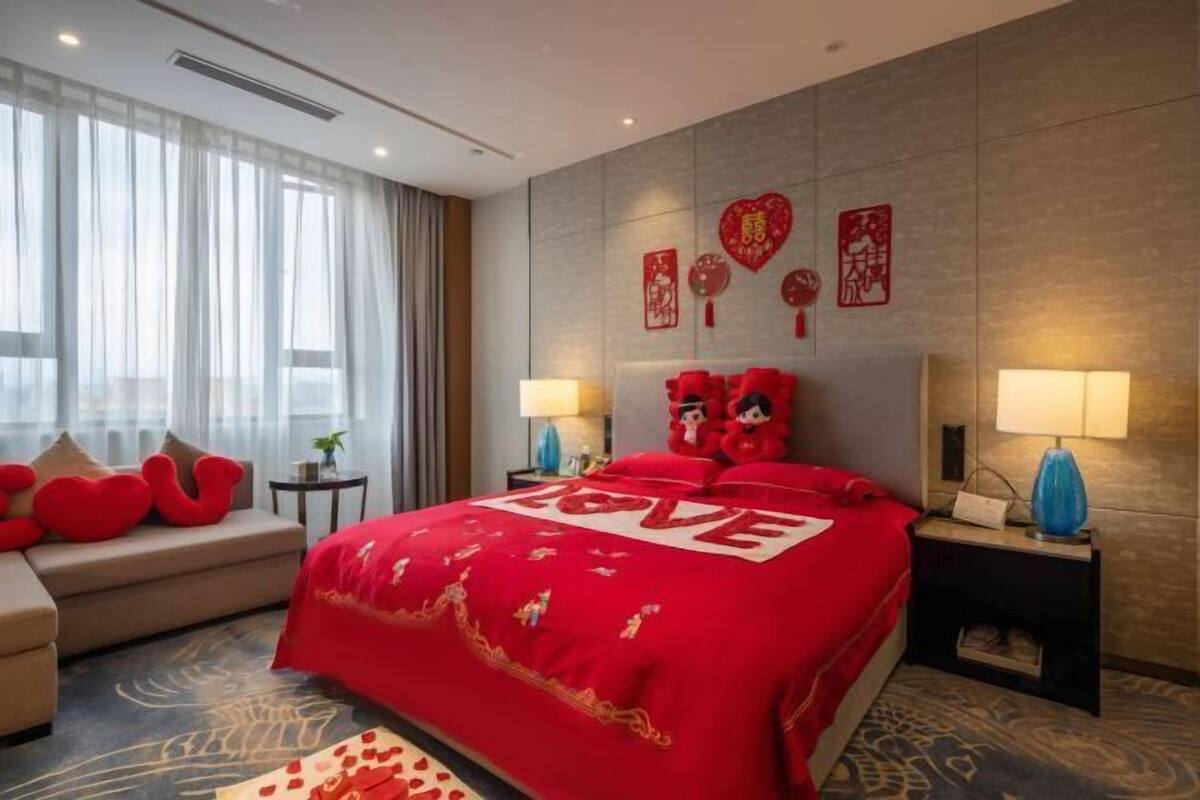 A hotel room with a large bed, a sofa, a nightstand, and a wall with decorative elements.