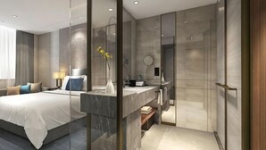 Een moderne hotelkamer met een bed, nachtkastje en een glazen scheidingswand tussen slaapkamer en badkamer.