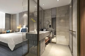 Une chambre d’hôtel moderne équipée d’un lit, d’une table de chevet et d’une cloison en verre séparant la chambre à coucher de la salle de bain.