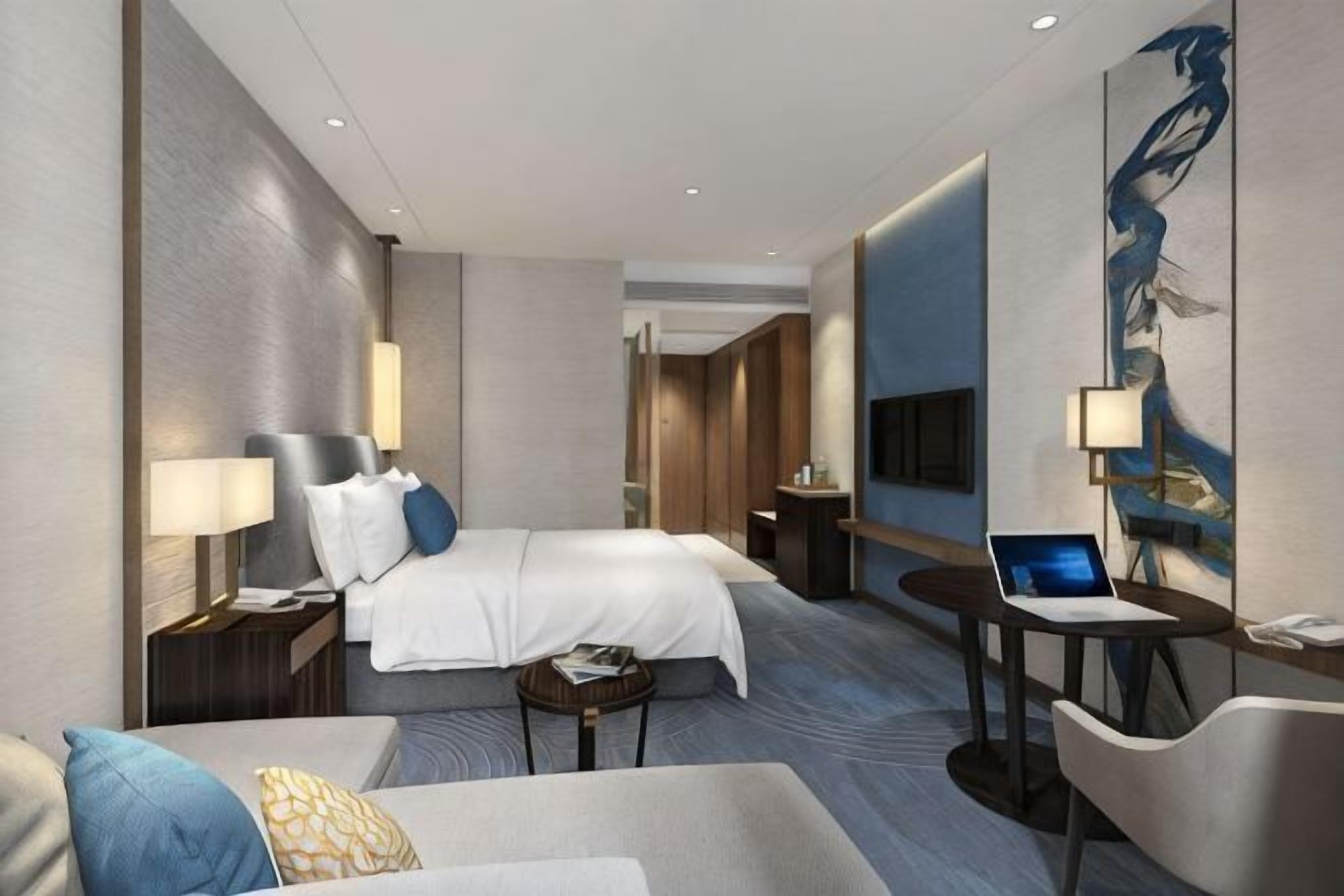 Une chambre d’hôtel moderne équipée d’un lit, d’un bureau avec un ordinateur portable, d’une chaise, d’un canapé et d’une télévision.