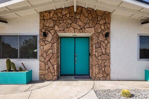 A turquoise double door with a stone archway, a cactus planter to the left, and a small cactus to the right.
