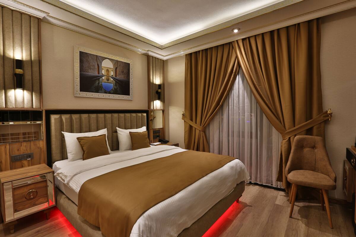 A hotel room with a large bed, a wooden nightstand, a chair, and a painting on the wall.