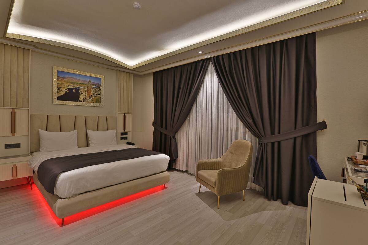 A modern hotel room with a large bed, a chair, a desk, and a painting on the wall.