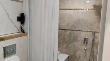 A bathroom with a toilet, a shower, and a marble wall.