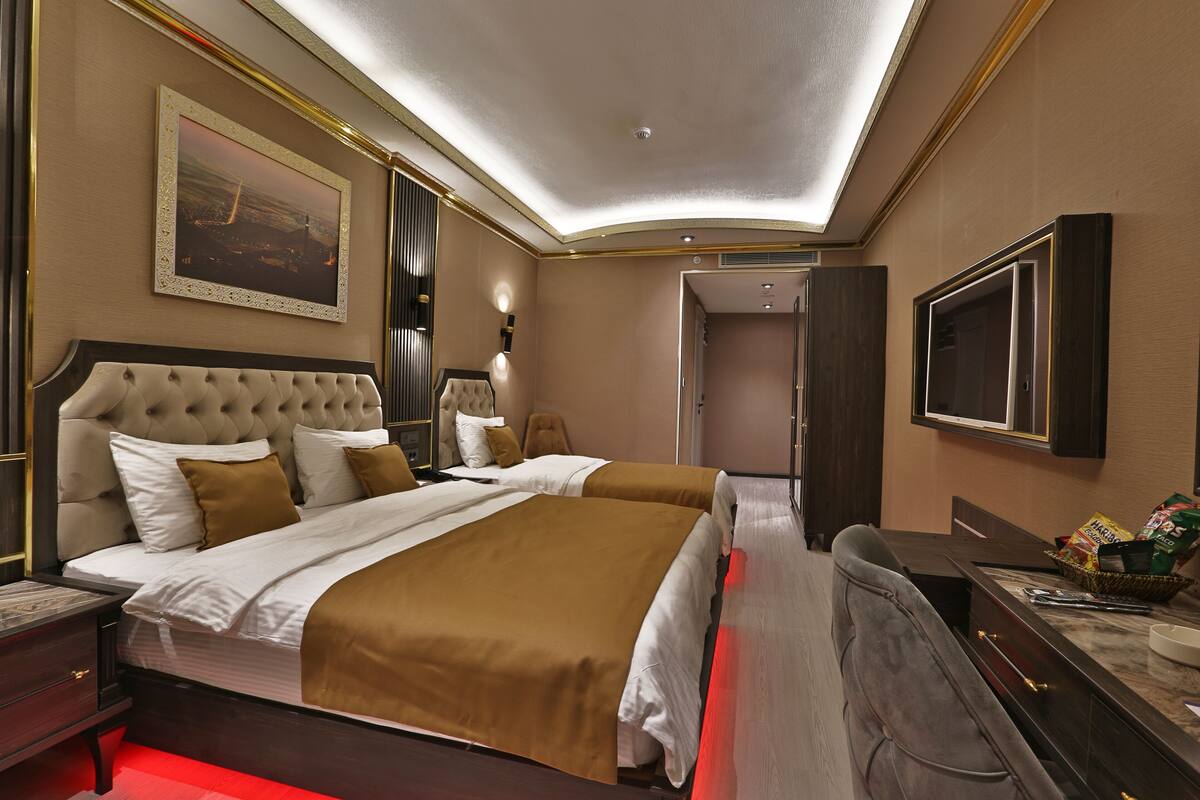 A modern hotel room with a large bed, a TV, and a desk with a basket of snacks.