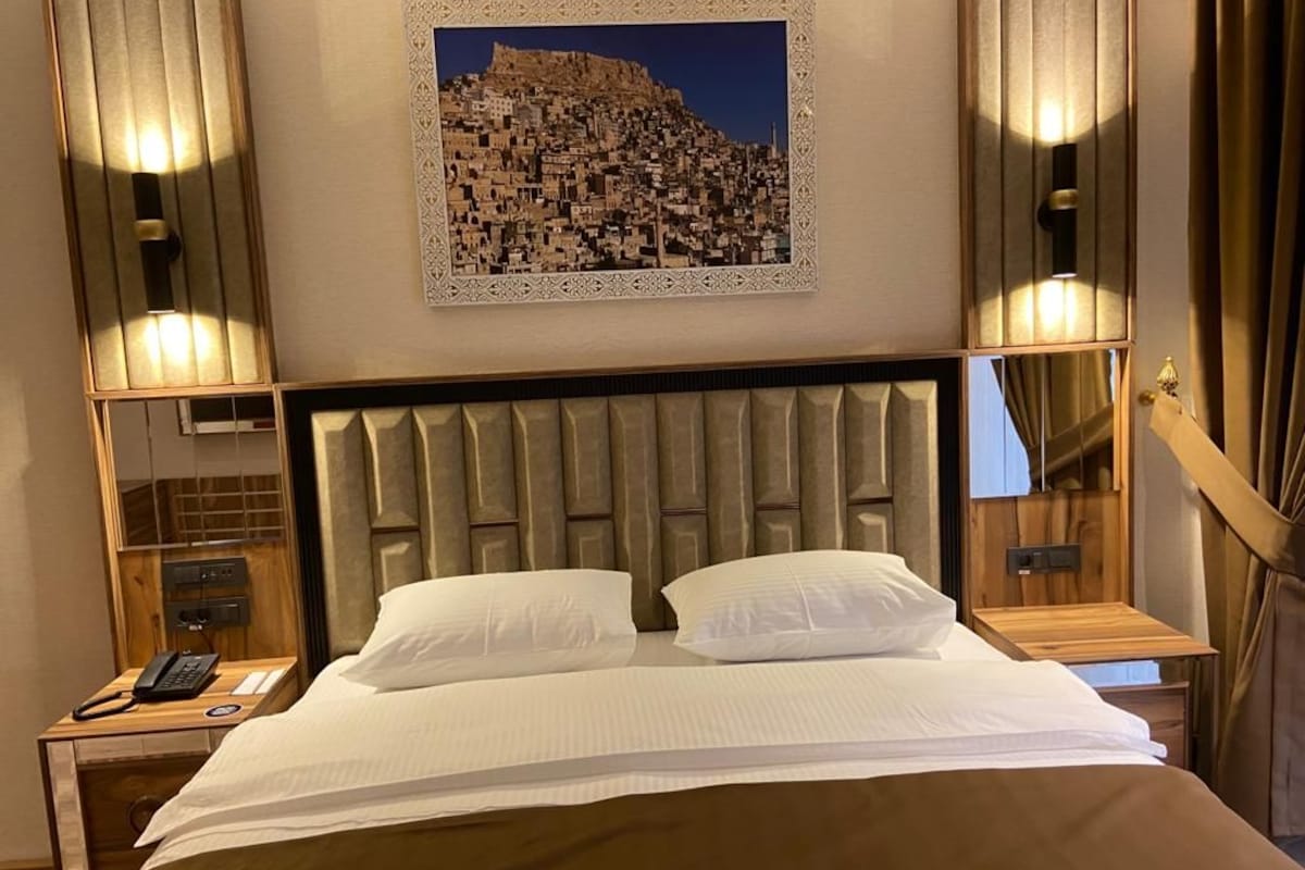 A hotel room with a large bed, a headboard, bedside tables, a telephone, and a framed picture on the wall.