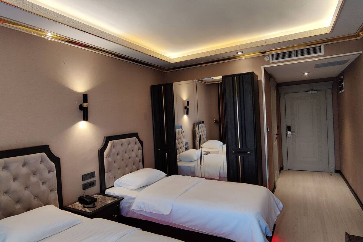 A hotel room with two beds, a bedside table with a phone, a mirror, and a TV.